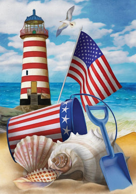 Lighthouse with American flag, beach toys, and shells on a sandy beach.