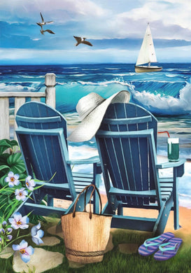 Beach scene with two blue chairs, a hat, and a bag on a wooden deck overlooking the ocean.